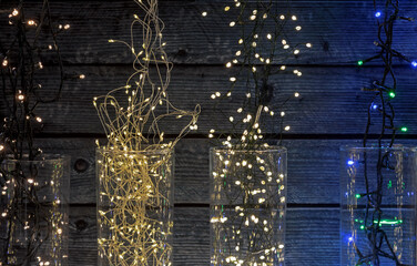 Christmas electric garlands in glass vases on a wooden background.