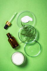 Cosmetic laboratory concept. Glass petri dish with cosmetic products, cream jar, serum bottle and green plants. Flat lay image.