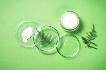 Cosmetic laboratory concept. Glass petri dish with cosmetic products, cream jar and green plants. Flat lay image.