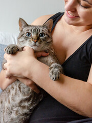 happy woman holding a cat indoors, sitting on a couch	
