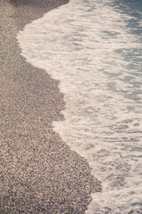 The beach of the Mediterranean coast with waves of azure water. Summer sea breeze. Seashore in sunny weather. Selective focus