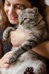 happy woman holding a cat indoors, sitting on a couch   © graziella