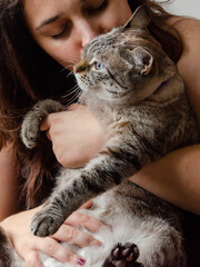 happy woman holding a cat indoors, sitting on a couch	
