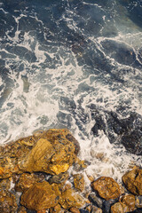 Wonderful views of the blue Mediterranean Sea. Sunny rocks, waves with foam and splashing water. The wave crashes into the rocks on the shore