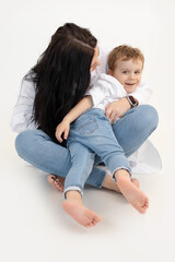Vertical of black haired woman and little boy, hugging, having fun together. Cuddling, sitting close. White background.
