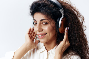 Smiling Curly Pretty Latin Woman in White Shirt In Headphones Looking At Camera Isolated At White Studio Wall Background. Music Devices DJ Technology Huge Sale Concept. Close Up Portrait. Copy Space