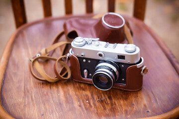 A vintage retro soviet camera in a leather case lies on a wooden background. Viennese chair in the...