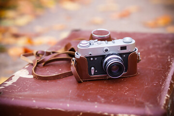 A vintage retro soviet camera in a leather case lies on a wooden background in the autumn park....
