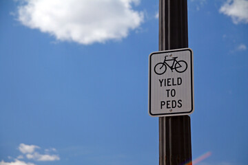 Yield to Peds sign hanging on a black pole with bicycle icon