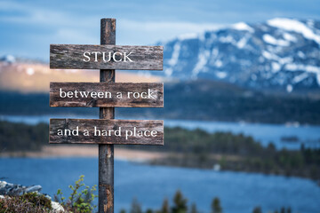 stuck between a rock and a hard place text quote written on wooden signpost outdoors in nature with...