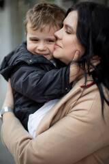 Vertical photo of middle aged black haired woman with close eyes, mother carrying son outdoors....