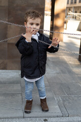 Vertical photo of cute little boy in black jacket standing on the street, holding chains....