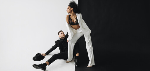 European man in a black suit hugs the leg of a young african american woman with curly hair on a black white background - Powered by Adobe