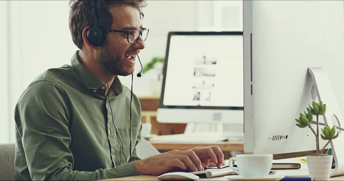 I can work like this all day. 4k video footage of a cheerful young businessman working on his computer while listening to music through his headphones in the office.