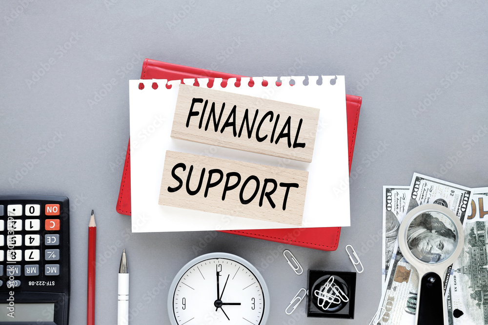 Poster financial support. text on wooden blocks on an open notebook on a gray background.