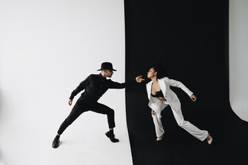 Fototapeta na wymiar European man in black suit on a white background dancing with young african american woman with curly hair on a black background