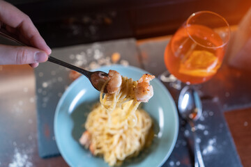 person eats italian carbonara pasta with seafood, shrimps, aperol spritz glass