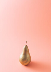 Golden pear against soft pastel pink background.Creative summer background concept, with copy space for text.