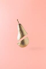 A golden pear cut in half floats in the air.Isolated on pink pastel background.Creative summer food fruit concept.