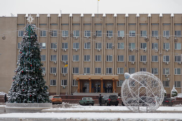 City square with administrative building and decorated christmas tree, Ukrainian flag, cars and...