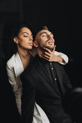 Photo of romantic multiethnic couple hugging together while standing on black studio