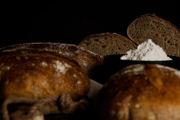 horizontal photo of artisan breads cut from wholemeal flour with jar of flour on rustic wooden table and black background