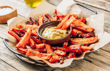Sweet potato fries on a metal tray with mustard sauce on wooden rustic background.
