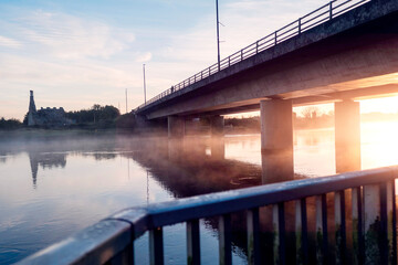 Sun rise over a river. Bridge and small castle in the background. Warm and cool color tone. Corrib river, Galway city, Ireland. Amazing nature scene. Mist over the water and sun flare.
