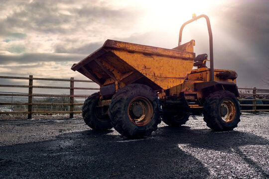 Old rusty dumper track parked on a parking lot in a country side. The vehicle is yellow color has many scratches. Warm sunny day. Dramatic sky. Construction and repair equipment for rent concept.