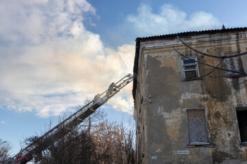 Firefighter works on boom of fire engine. Fireman on sky background. Burning old building in the...