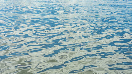 Abstract image of light reflections on the water’s surface, producing a dappled pattern of blue, green and grey.
