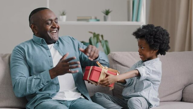 Little loving cute daughter congratulates dad on birthday gives gift adult man closes eyes in anticipation of surprise surprised amazed enjoys express gratitude hugs child Happy Father day celebration
