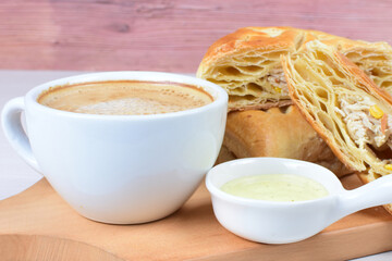 Chicken and cheese puff pastry, accompanied by corn sauce and a cup of Colombian coffee on a wooden background