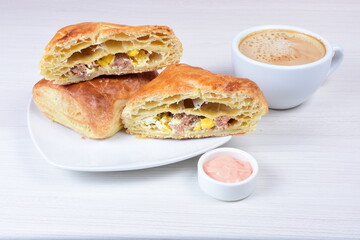 Ham and corn puff pastry, accompanied by sauce on a wooden background