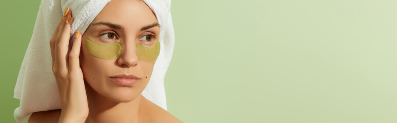 Woman in sunlight with eye patches on pastel green background. Morning skincare routine