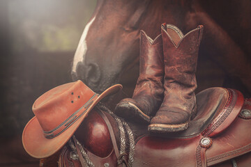 Ranch scene: Western boots and a cowboy hat on a western saddle in front of a horse - obrazy, fototapety, plakaty