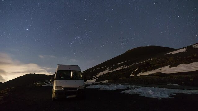 Time lapse of night sky and fog over Etna vulcano mountain with camper van in foreground in winter time, Sicily, Italy