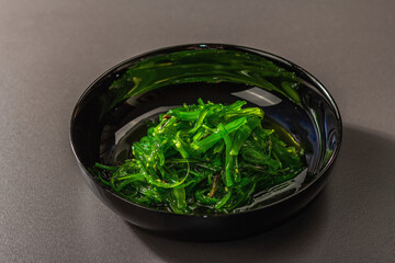 Wakame seaweed salad with sesame seeds and chili pepper in a bowl. Trendy hard light, dark shadow