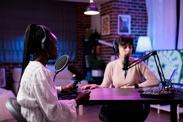Multiethnic team of women meeting in studio to chat on podcast, recording episode show with...