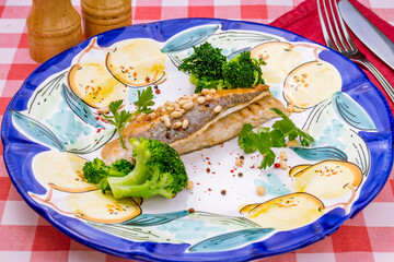 Fried sea bass with broccoli on plate on red italian table