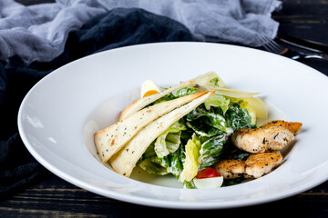 Salad caesar with chicken on white plate on black wooden table