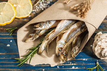 Sun-dried smelt in a paper package. Salted fish with marine decor. Lemon, fresh rosemary, sea rope