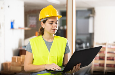 Woman construction worker standing and using laptop in building site.