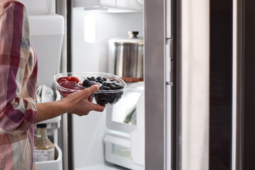 Woman taking container with fresh berries from refrigirator