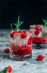 Raspberry lemonade in a glass with ice and fresh rosemary on a concrete background.