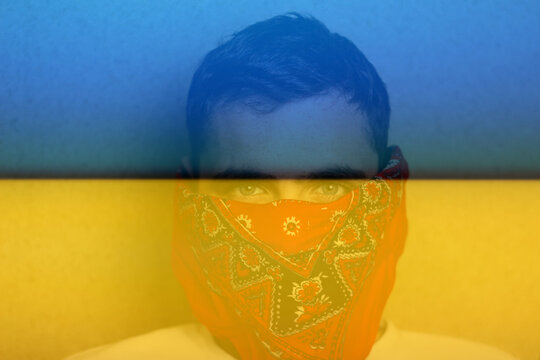 Flag Ukraine. Close-up portrait of young caucasian brown-haired man in red bandana on face at home looking at camera. Lifestyle. Handsome guy. Beige background. Gray eyes. Selective focus