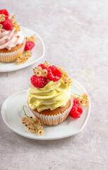 Delicious cupcakes with fresh raspberries and currants on Heart shaped white plates over light beige background.