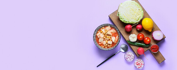 Bowl of tasty Mexican pozole soup and ingredients on lilac background with space for text