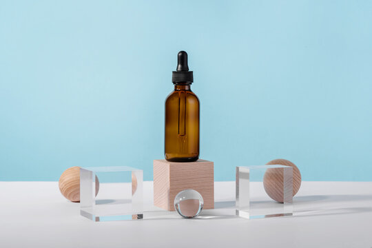 Oil cosmetics amber product packaging with stylish props. Serum cosmetic bottle with peptides and retinol on acrylic and wooden blocks on blue background. Serum dropper mockup on pedestal podium
