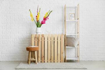 Chair and vase with beautiful gladiolus flowers near white brick wall